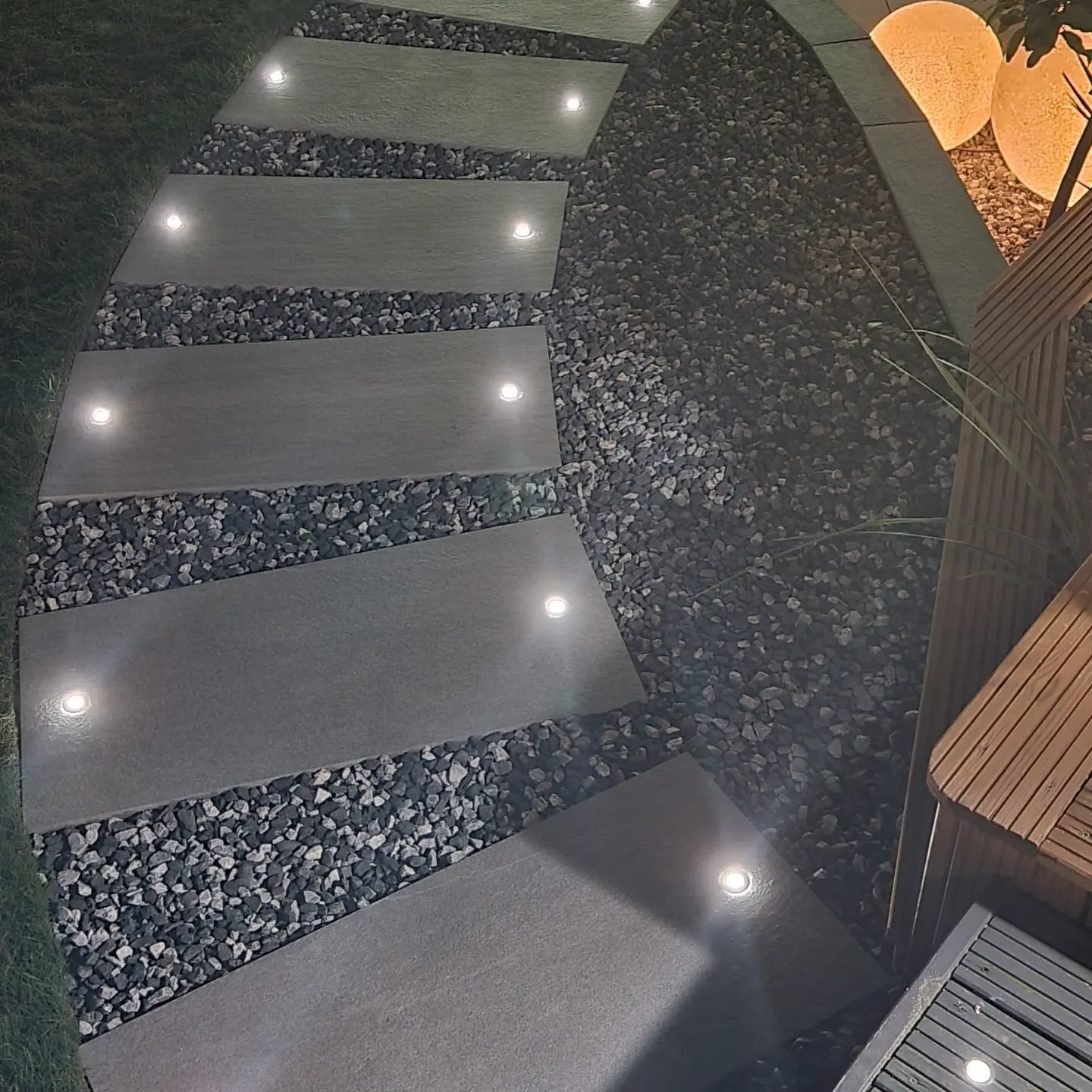 The same stepping slabs at night, each with two small lights set into it, glowing against the dark stone.