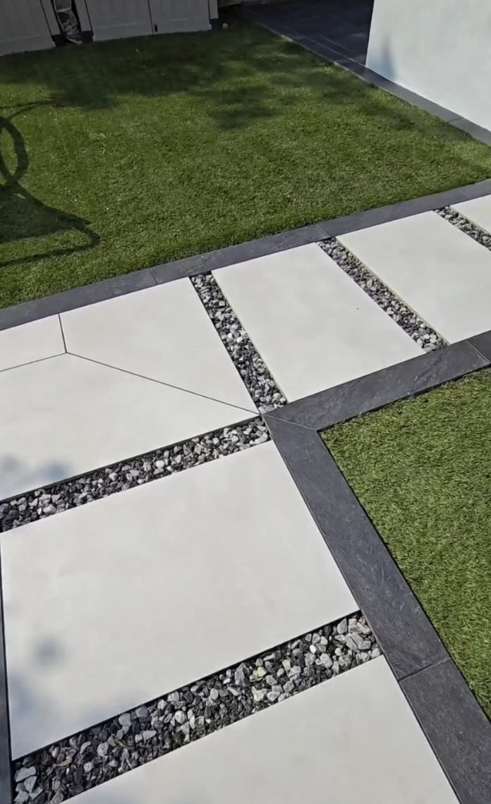 Large pale porcelain slabs with gravel joints, framed by a dark porcelain border against artificial lawn.