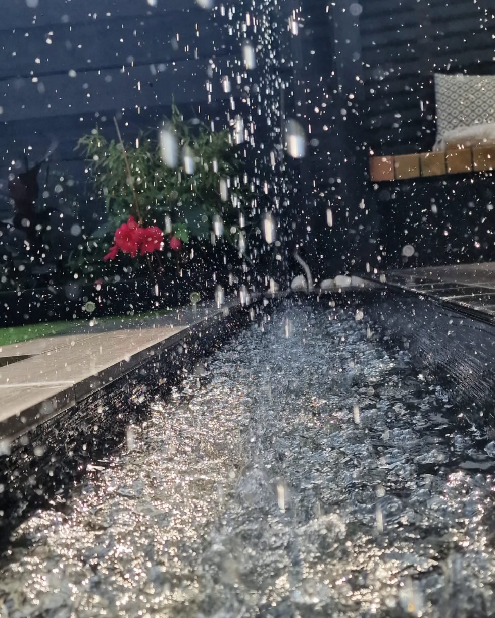 Water drops splashing into a dark pebble-filled rill at dusk.